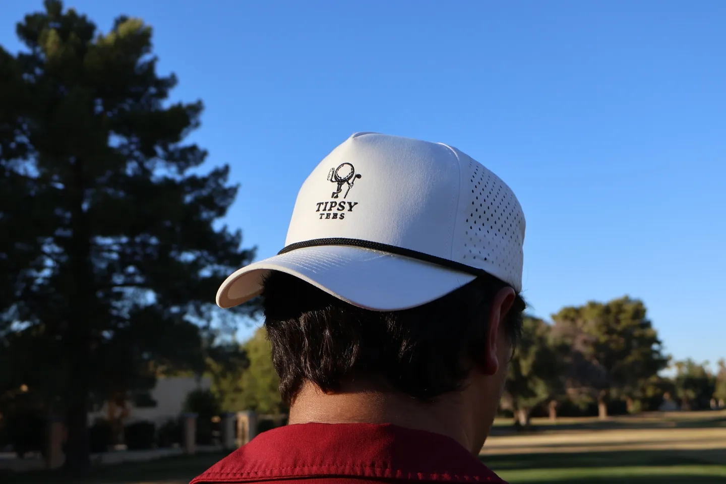 Person wearing a white cap outdoors with trees and blue sky.